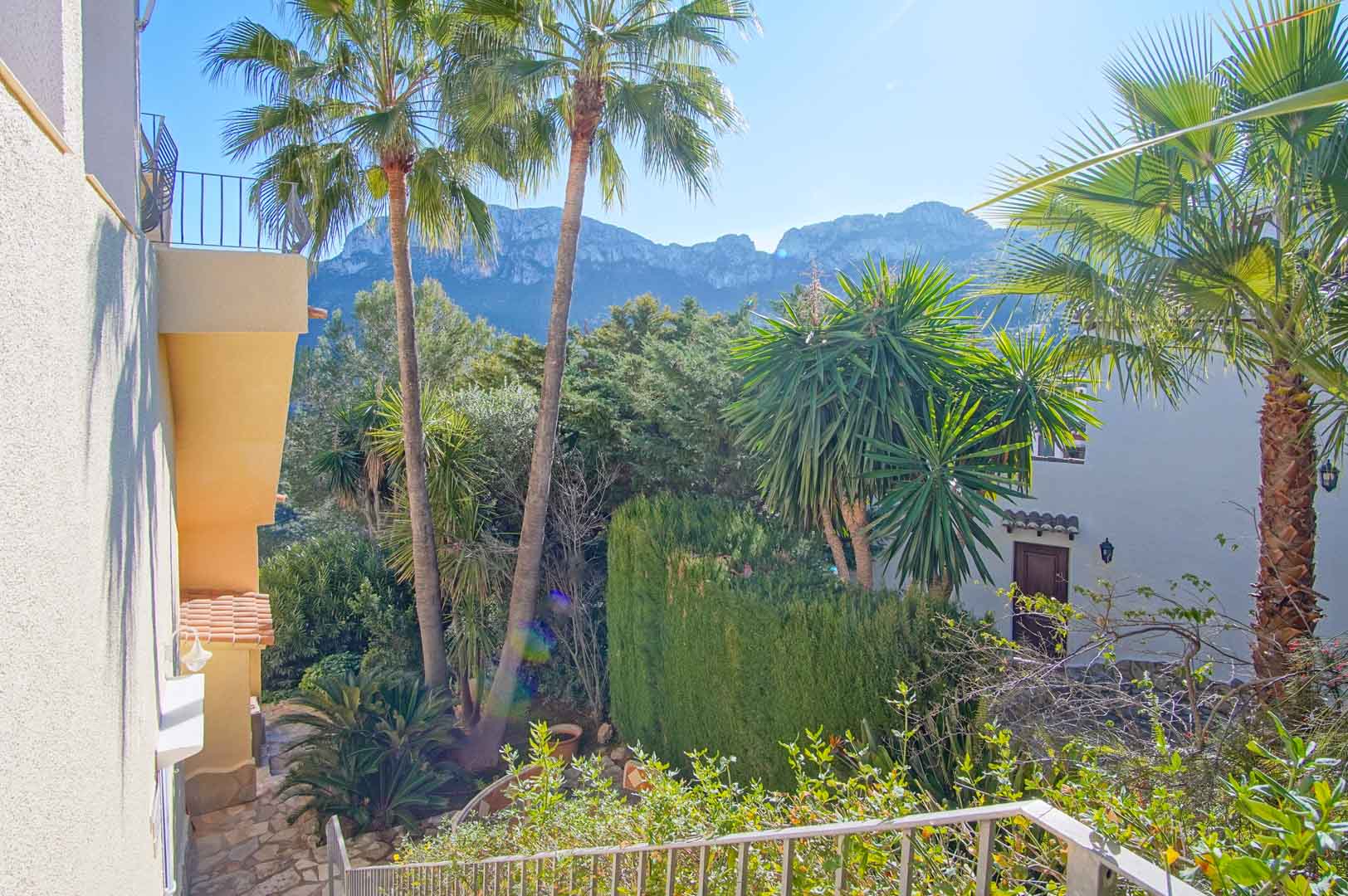 Elevated perspective from the outdoor stairs overlooking the mountain range, framed by mature palm trees and lush Mediterranean gardens.