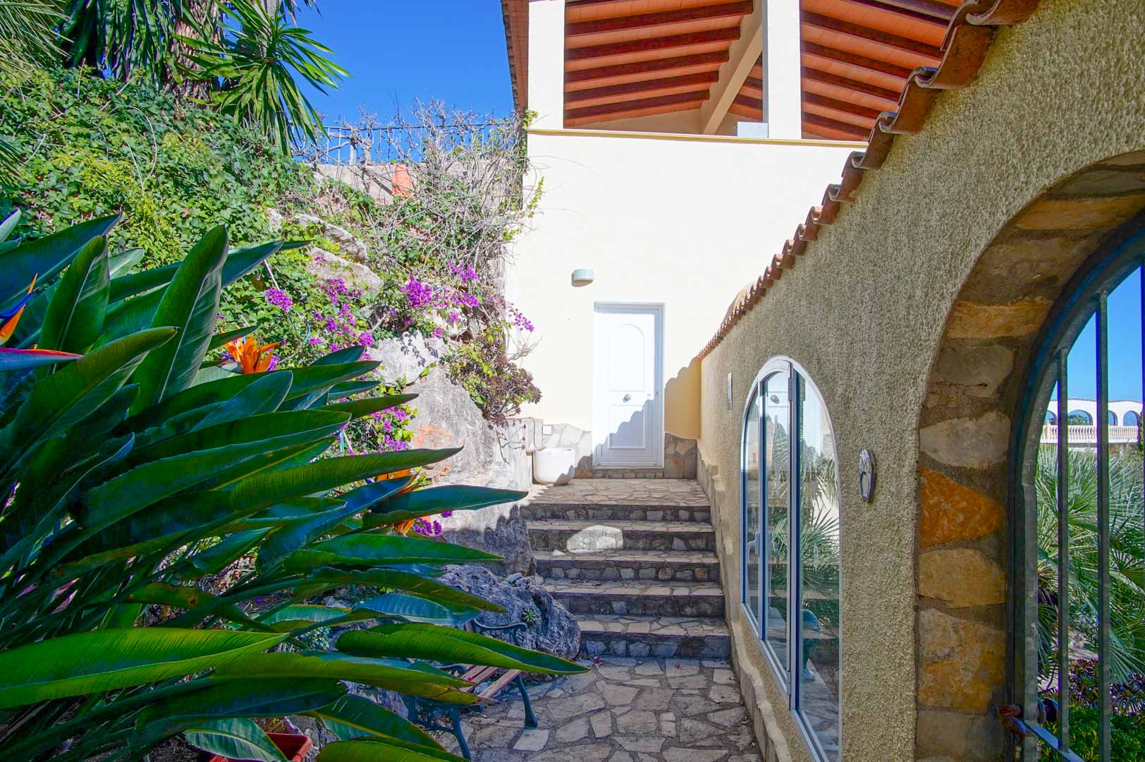 Exterior access featuring natural stone steps, Mediterranean landscaping, and rustic stone walls with arched windows.