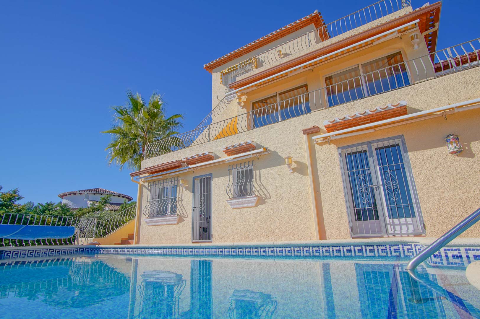 Exterior perspective of the three-story villa from the pool, showcasing tiered terraces with wrought iron railings and traditional architecture.