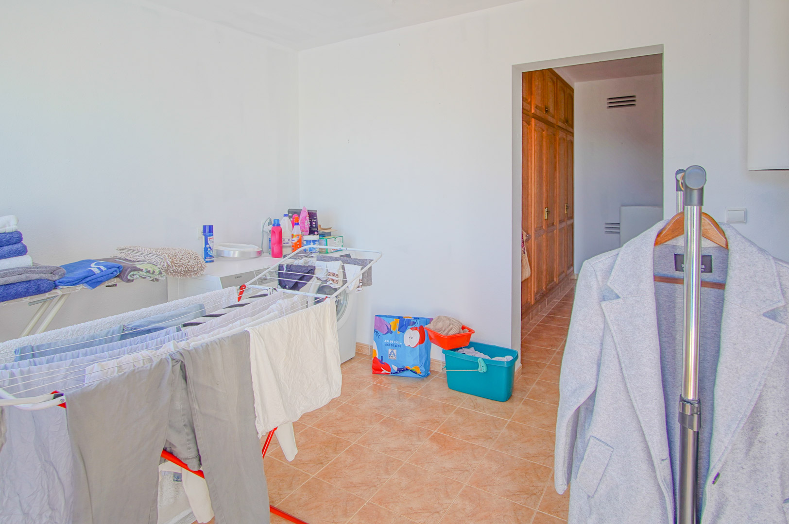 Functional laundry area featuring a washing machine, drying racks, and tiled flooring, with a doorway leading to built-in wooden wardrobes.