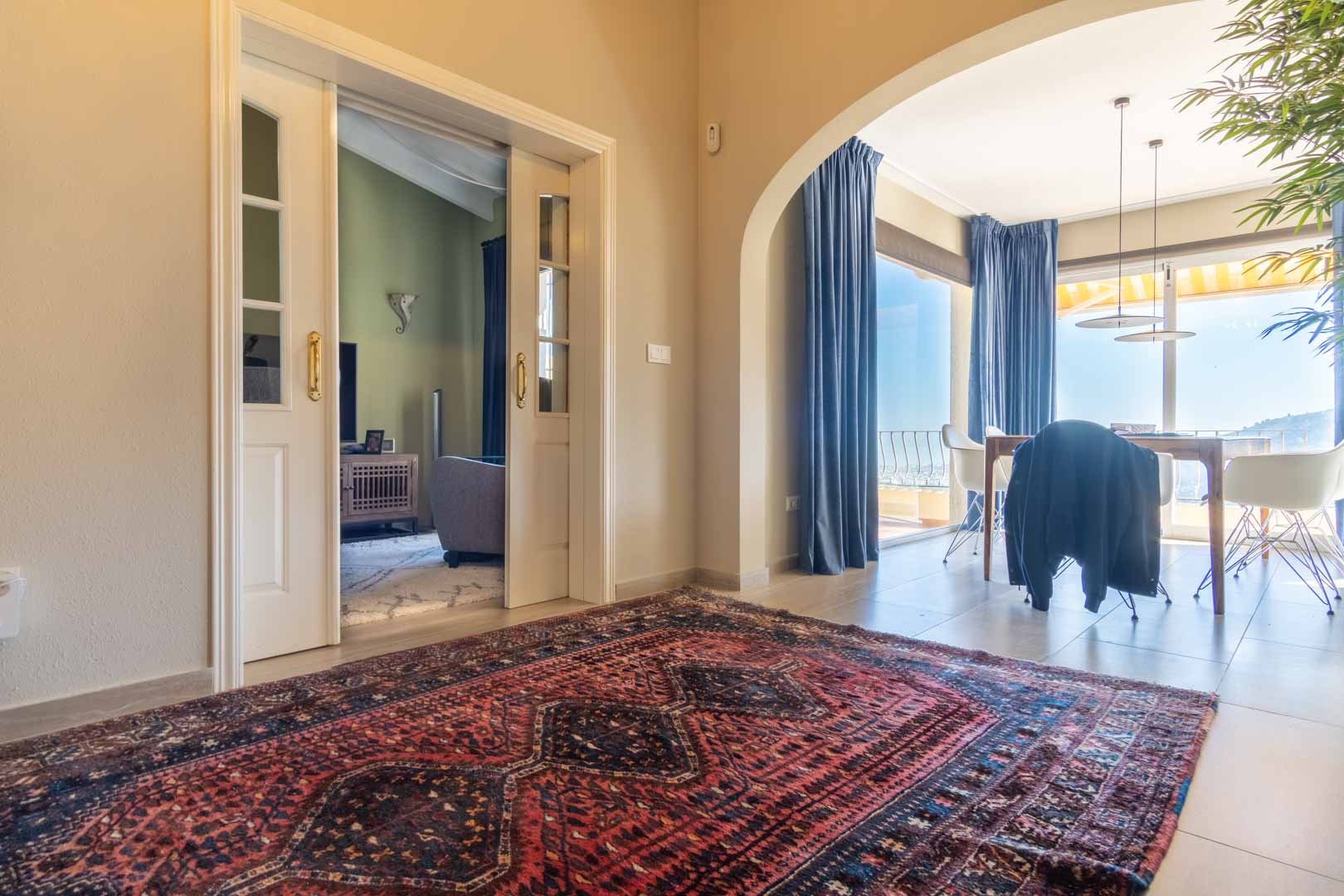 Hallway featuring a patterned rug, white sliding glass doors leading to the lounge, and an arched entrance to a dining area with panoramic sea views.