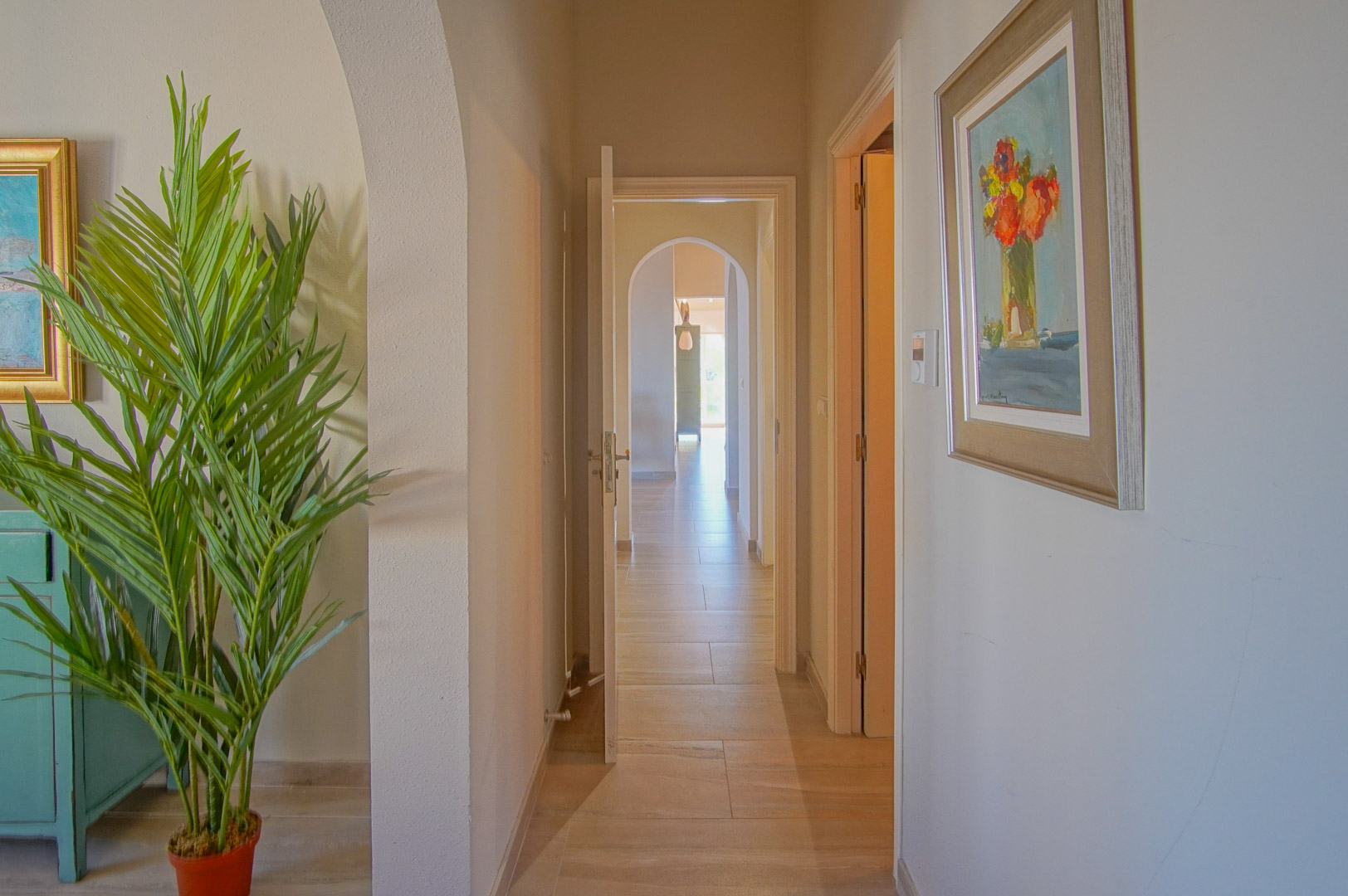 Interior hallway featuring ceramic tile flooring, decorative arches, and neutral-toned walls. The perspective shows a sequence of doorways illuminated by natural light.