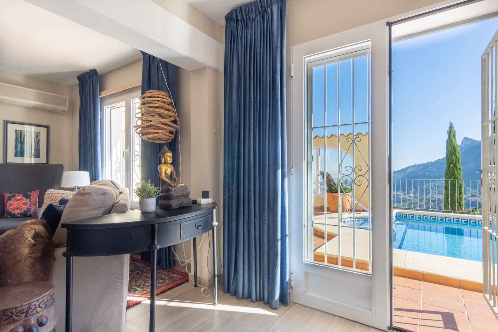 Living space featuring blue velvet curtains and a console table, with direct access to the pool terrace and panoramic mountain views.