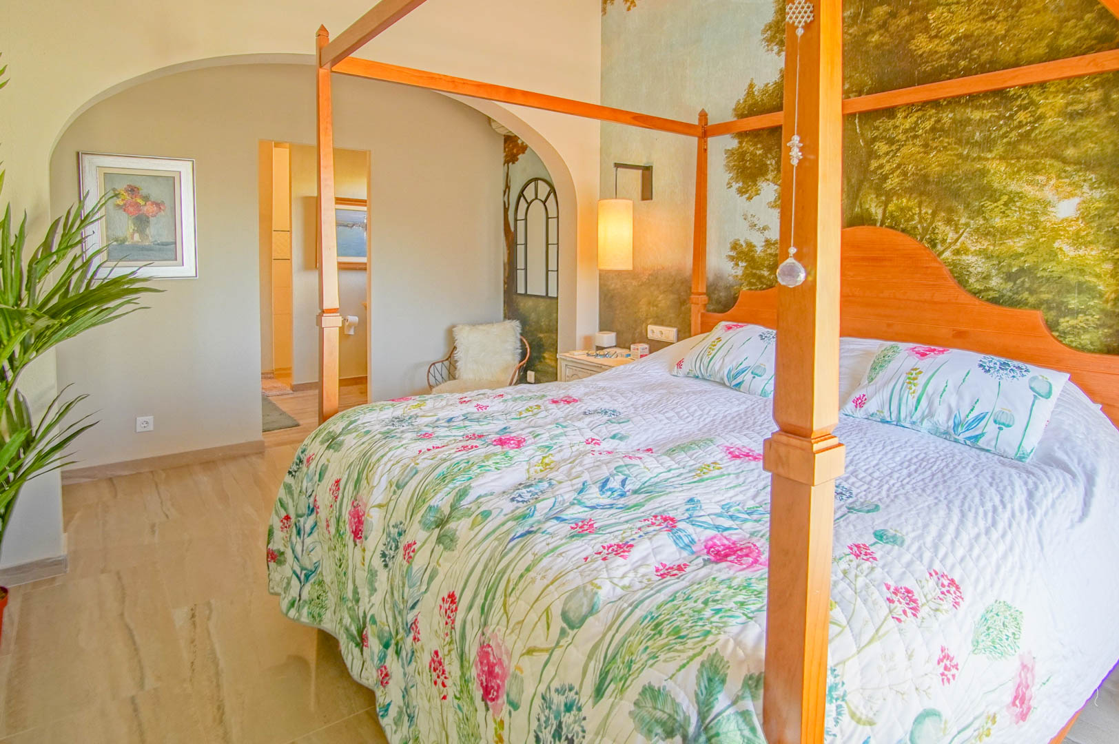Master bedroom featuring a wooden four-poster bed, landscape mural wallpaper, and polished stone flooring. An architectural arch leads to the en-suite bathroom.