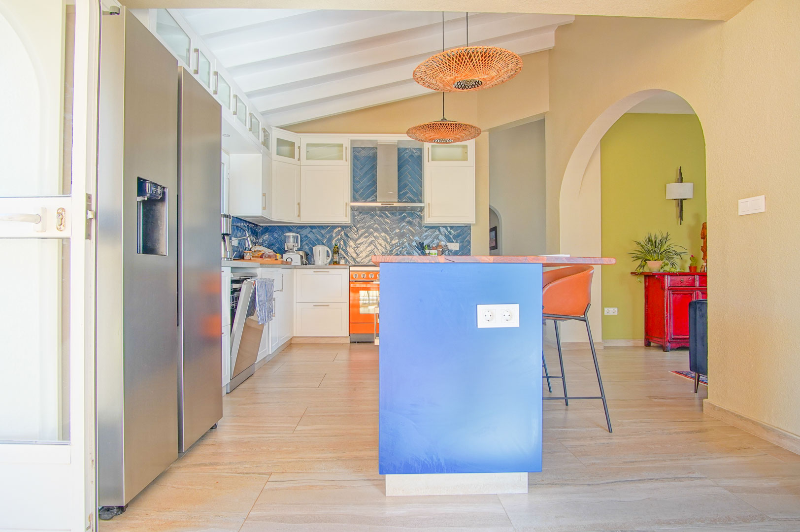 Modern kitchen featuring a blue island with wooden top, herringbone tile backsplash, and slanted beamed ceilings. Includes a side-by-side refrigerator and woven pendant lighting.