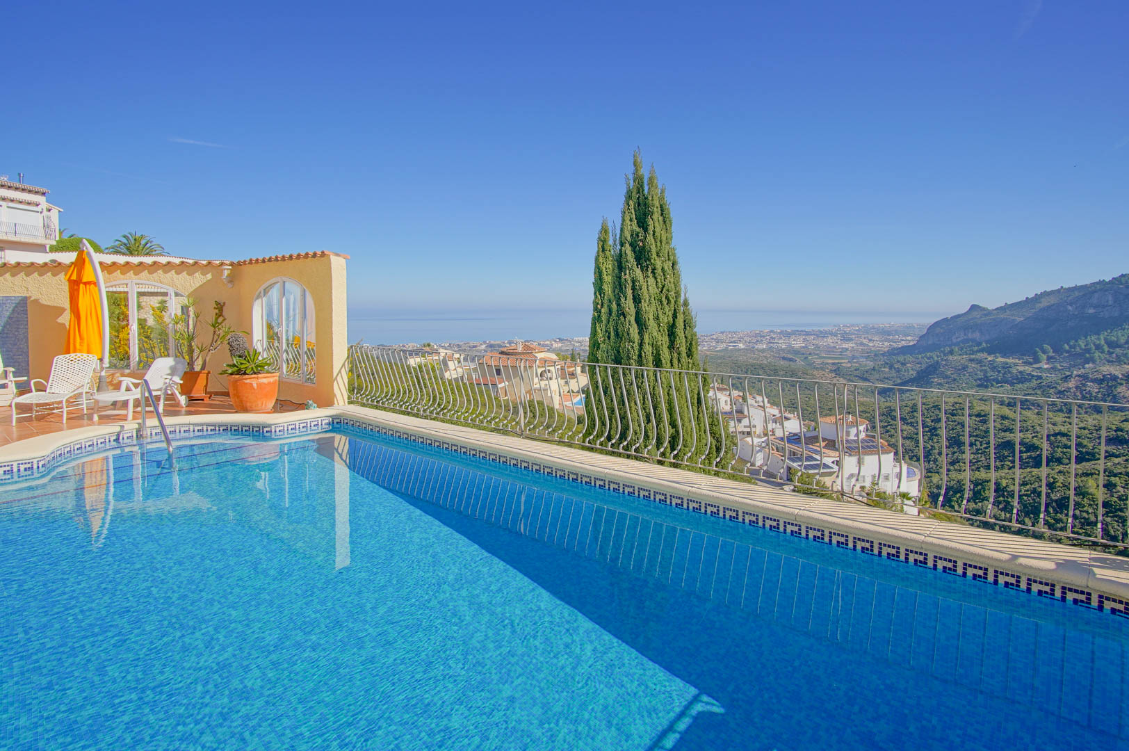 Outdoor swimming pool with blue mosaic tiling and a decorative border, offering panoramic views of the Mediterranean coast and surrounding mountains from the terrace.