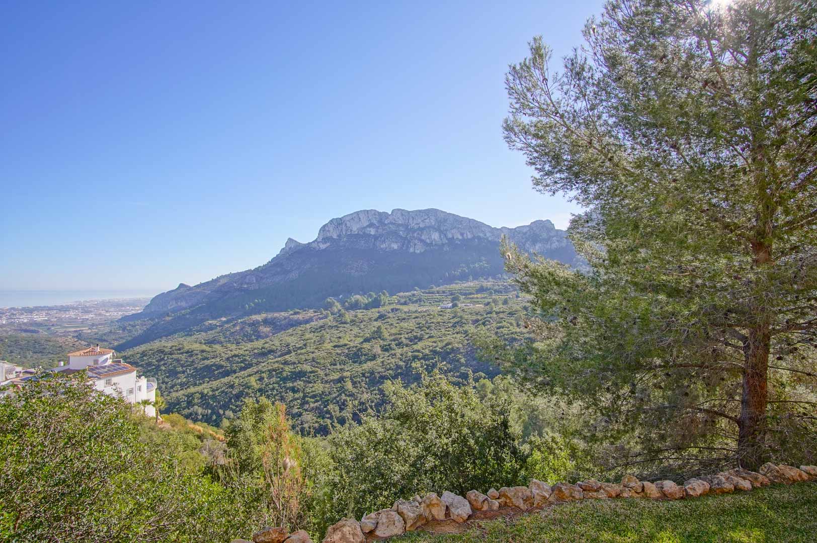 Panoramic mountain and valley views from the garden, featuring a natural stone border and mature pine trees overlooking the Mediterranean coastline.