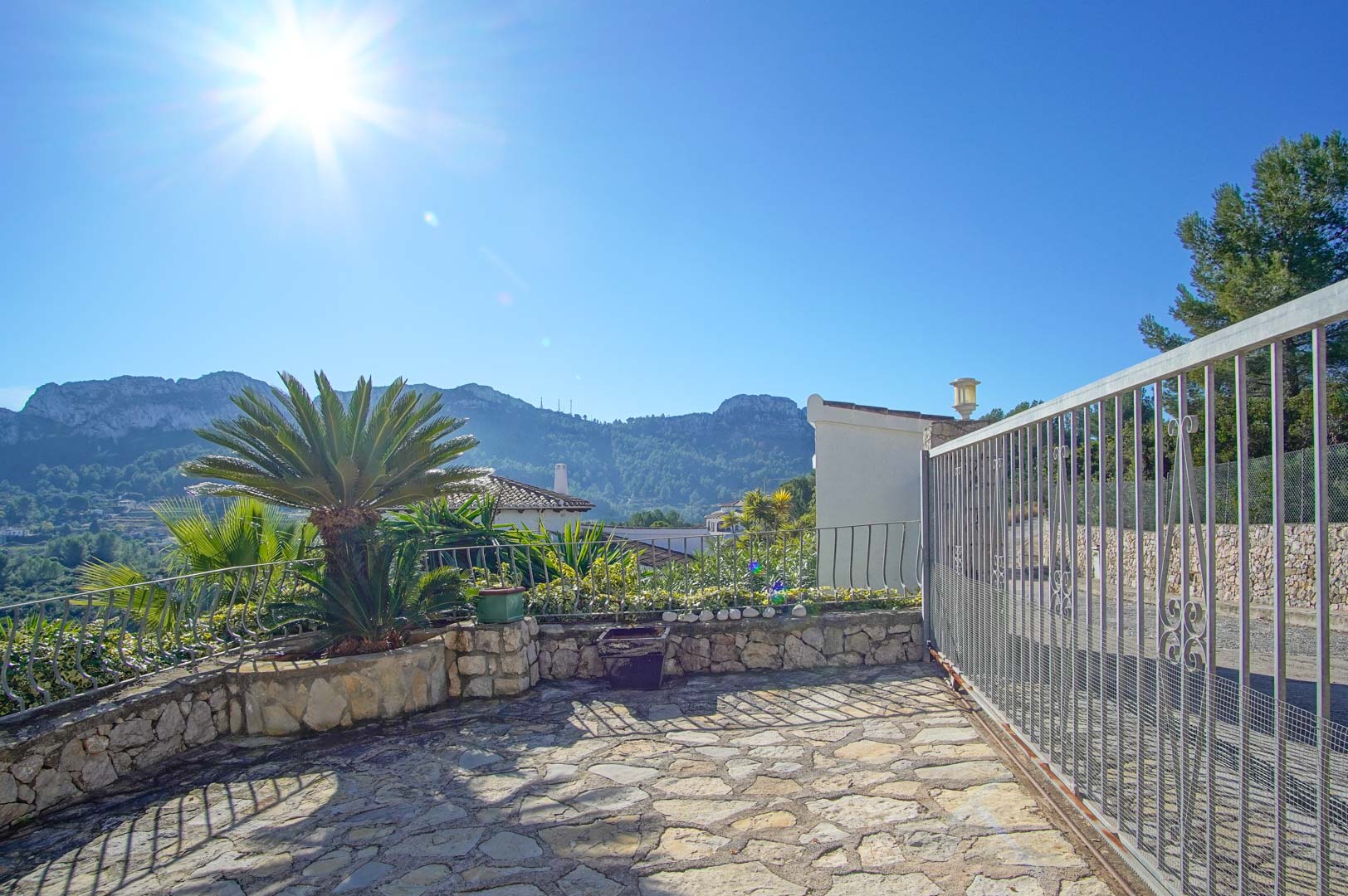 Property entrance featuring natural stone paving, a sliding metal gate, and panoramic mountain views under a bright, clear sky in Monte Pego.