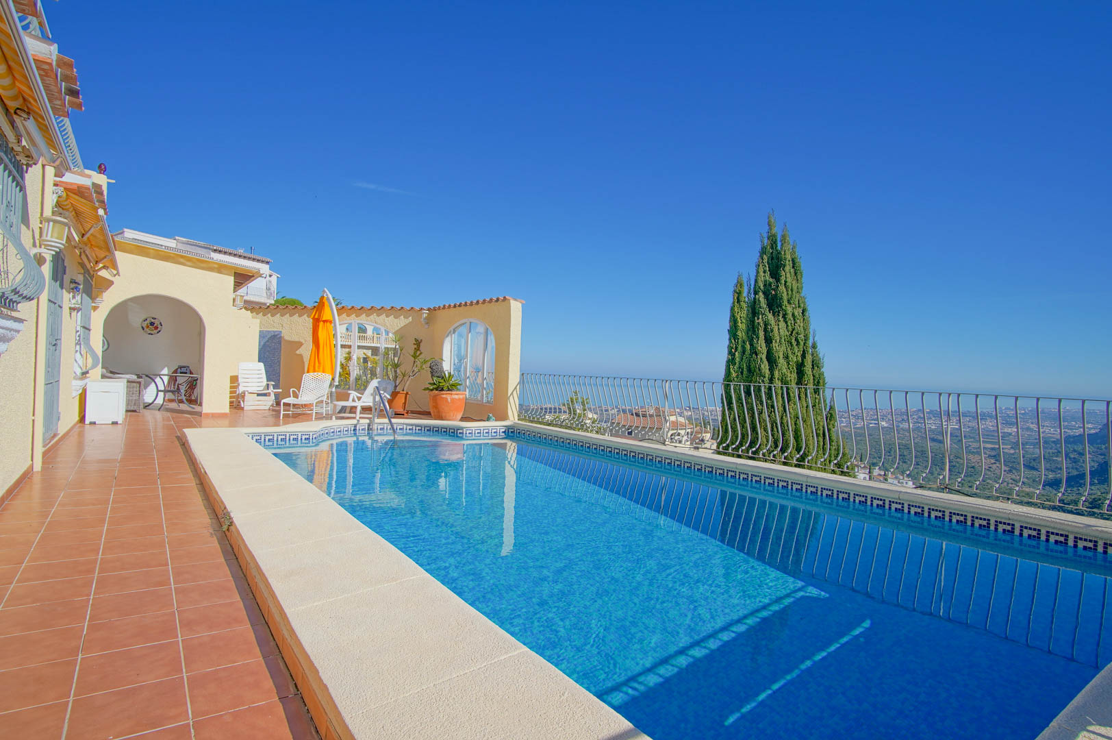 Rectangular pool with blue mosaic tiles and Greek key border, set on a terracotta terrace with panoramic Mediterranean and valley views.