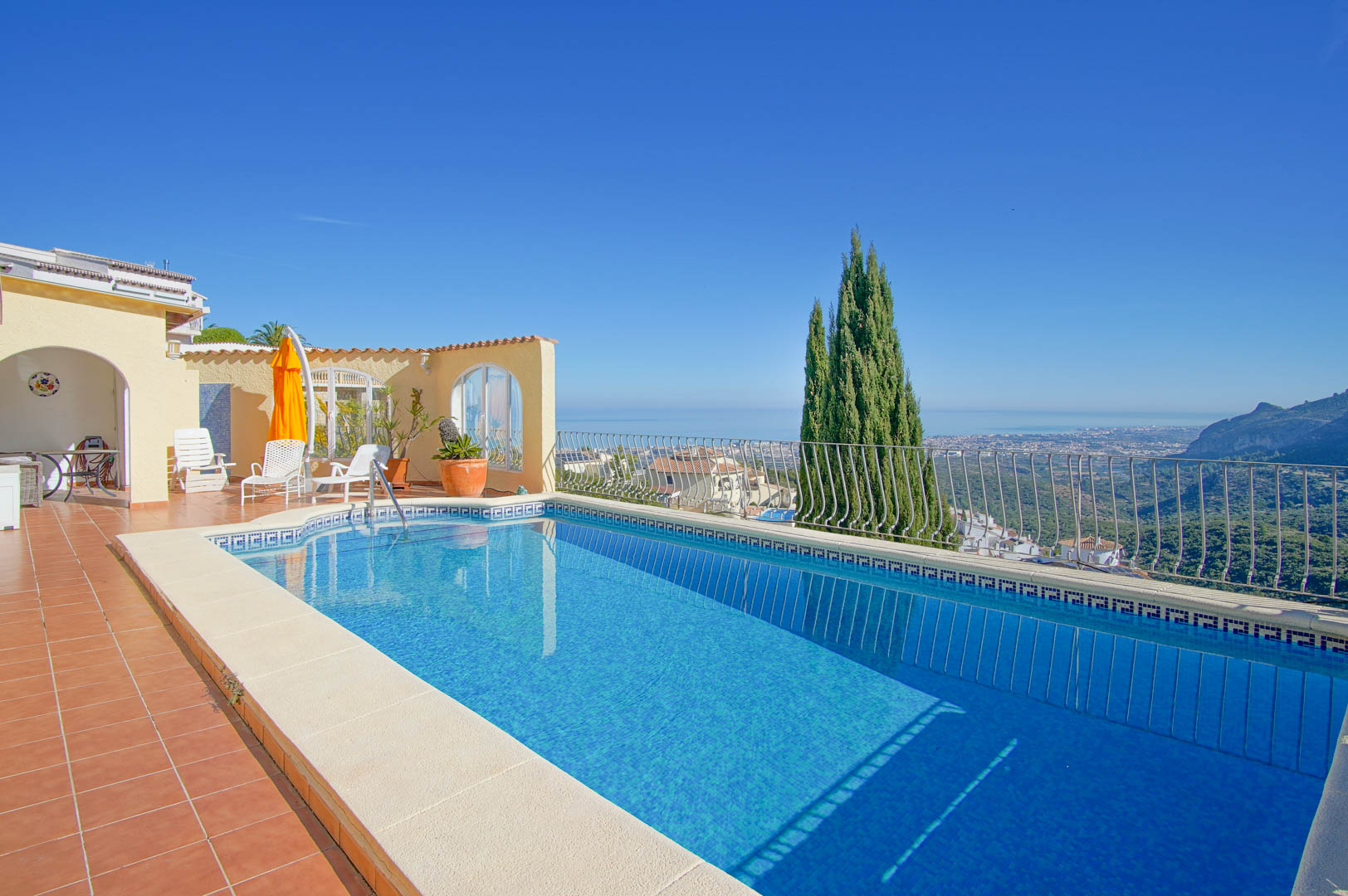 Rectangular swimming pool with blue mosaic tiling and terracotta terrace, offering panoramic views of the Mediterranean Sea and the coastal mountains.