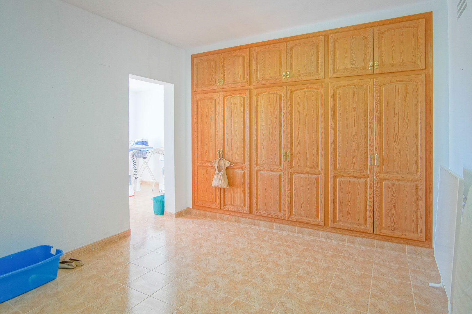 Room featuring a large built-in wooden wardrobe, ceramic tiled flooring, and an open doorway leading to the adjacent laundry area.