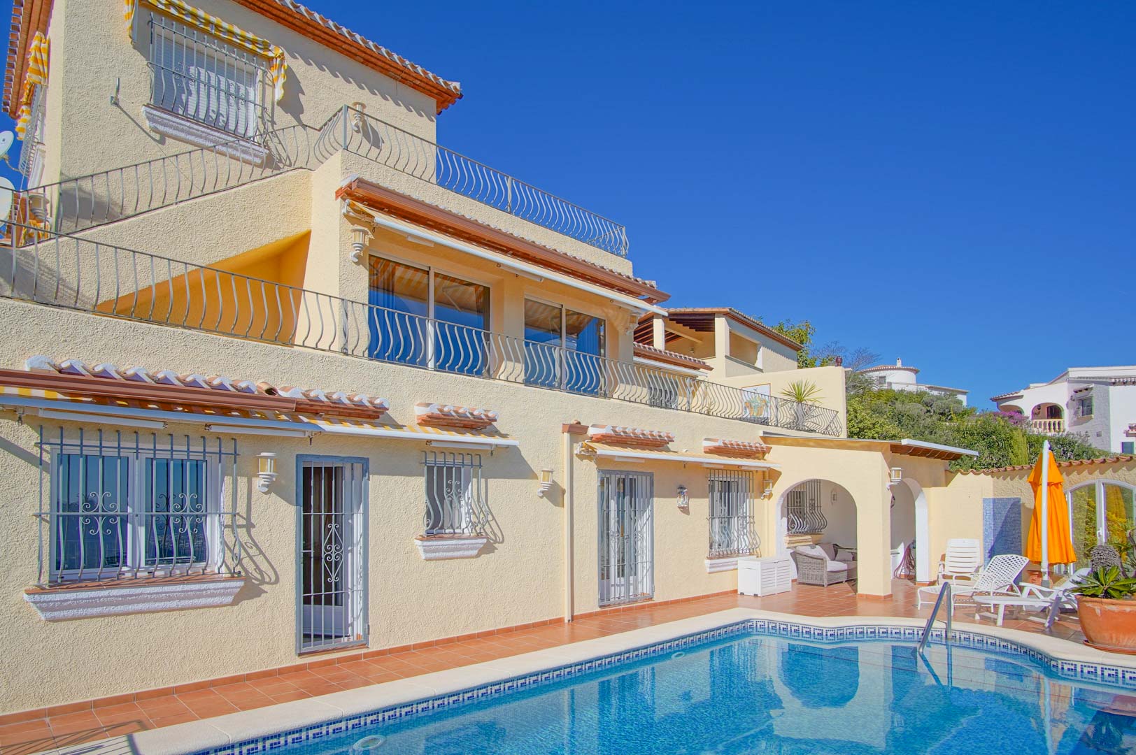 Three-level villa exterior featuring a mosaic-tiled pool, terracotta sun deck, and multiple terraces with decorative wrought iron railings.