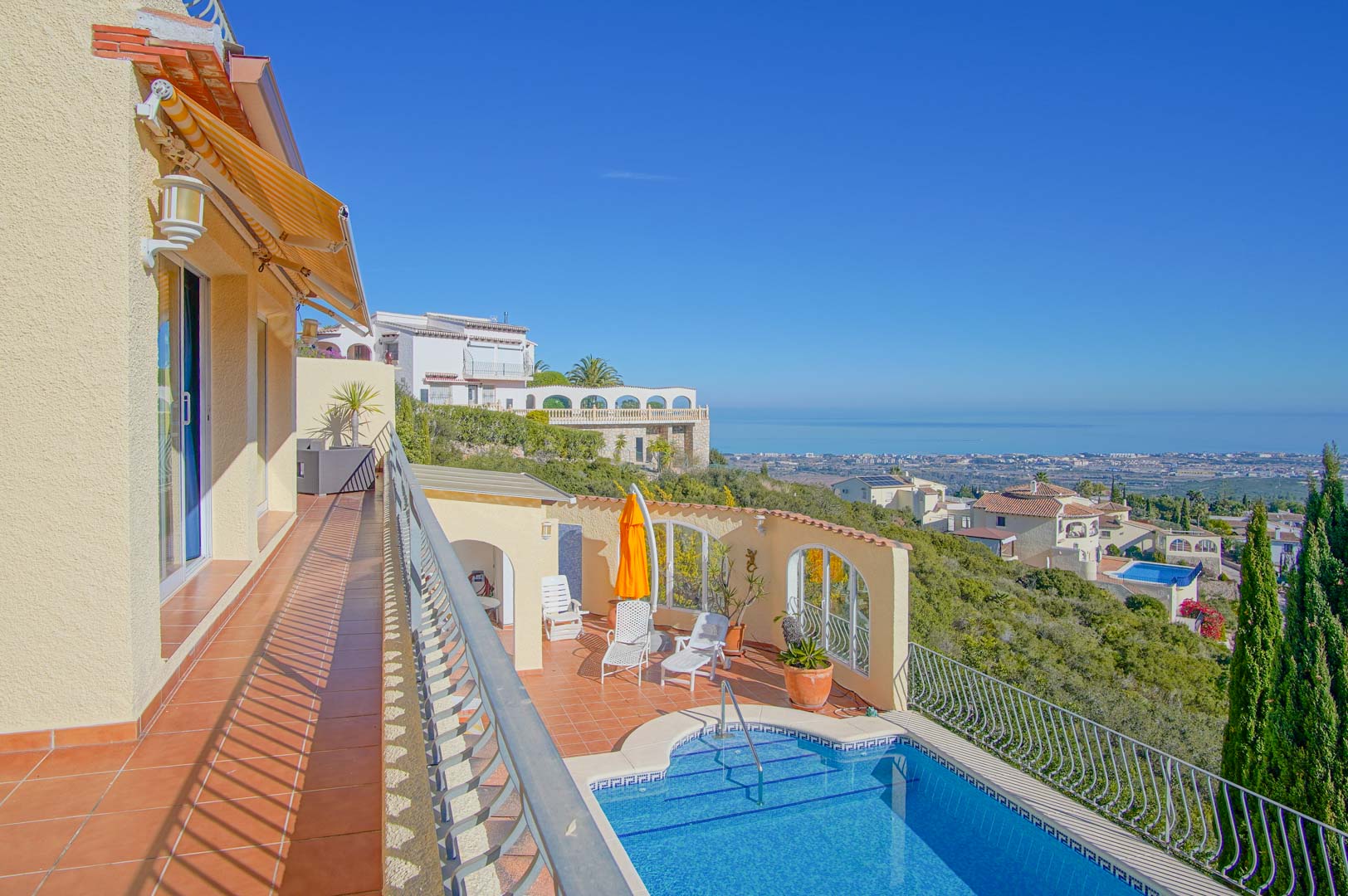 Upper terrace featuring terracotta tiling and a retractable awning, overlooking the private pool deck and expansive Mediterranean coastal views.