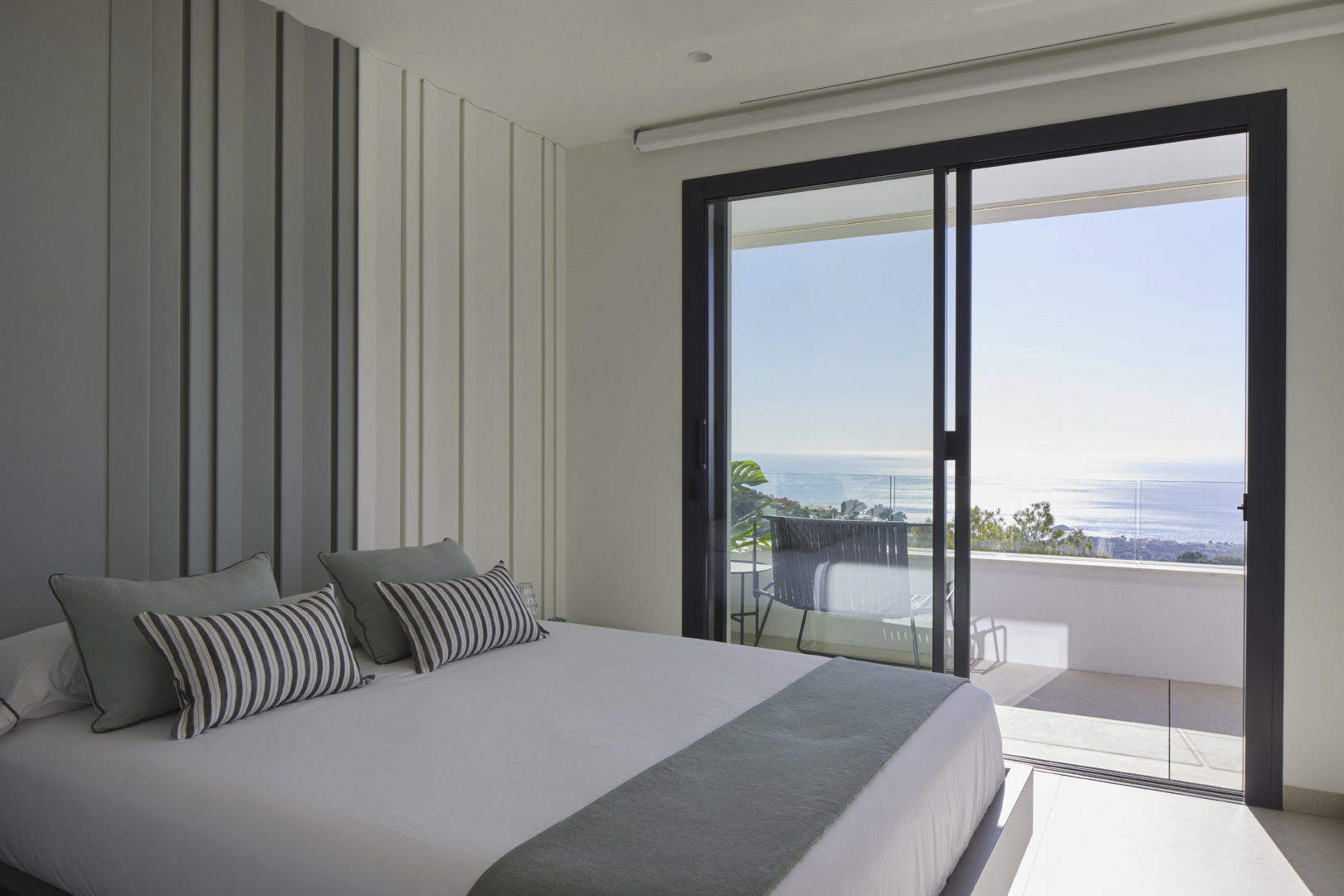 Bright bedroom featuring decorative vertical wall paneling and direct access to a private terrace with panoramic Mediterranean Sea views.