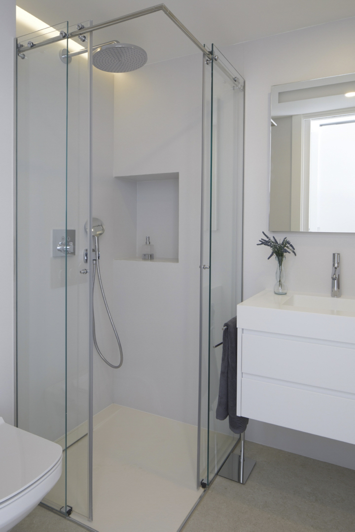 Modern bathroom featuring a glass-enclosed walk-in shower with a rain shower head and built-in niche. A floating white vanity with integrated sink and chrome fixtures completes the space.