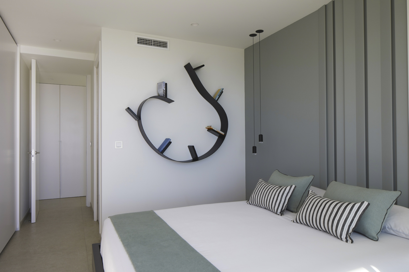 Modern bedroom featuring a unique curved black wall shelf, a grey paneled accent wall, and minimalist pendant lighting over the bed.