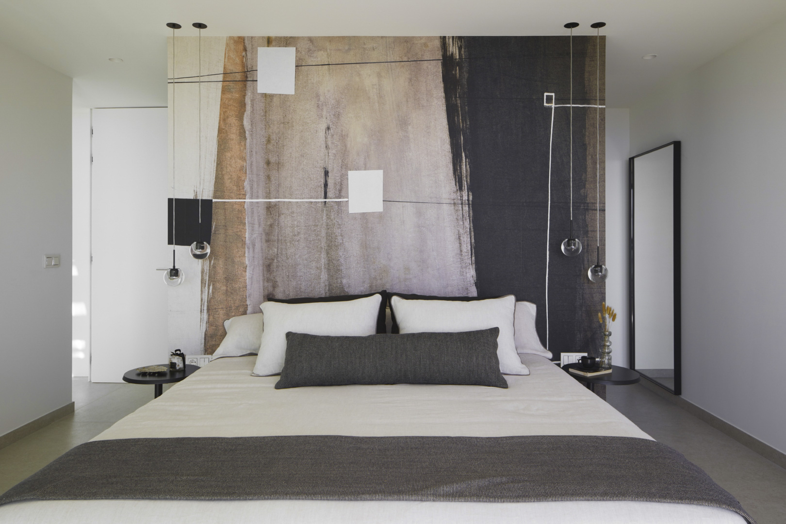 Modern bedroom featuring an abstract art mural headboard, minimalist pendant lighting, and sleek black side tables against a neutral color palette.