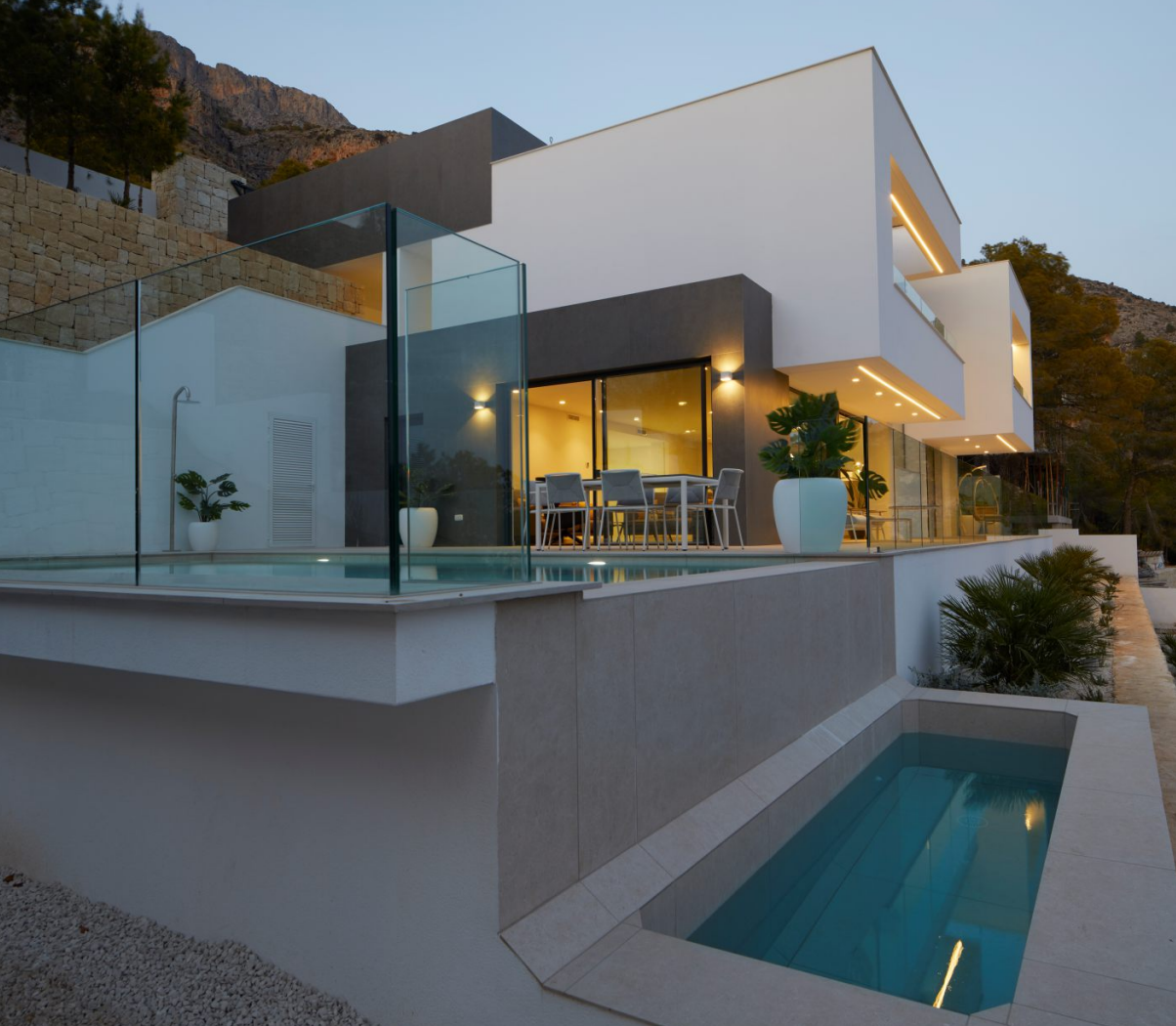 Modern exterior featuring an infinity pool with glass balustrades, multi-level terraces with integrated lighting, and a sleek white and anthracite facade.