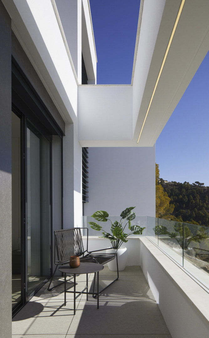 Private terrace featuring glass balustrades, minimalist outdoor seating, and mountain views. The white architectural overhang includes integrated linear LED lighting.