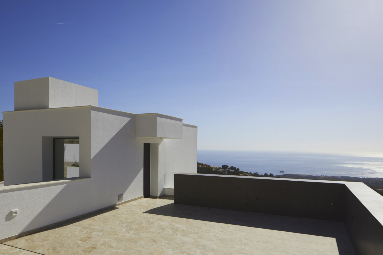 Upper terrace featuring minimalist white architecture, stone-effect tiling, and expansive panoramic views of the Mediterranean coastline.