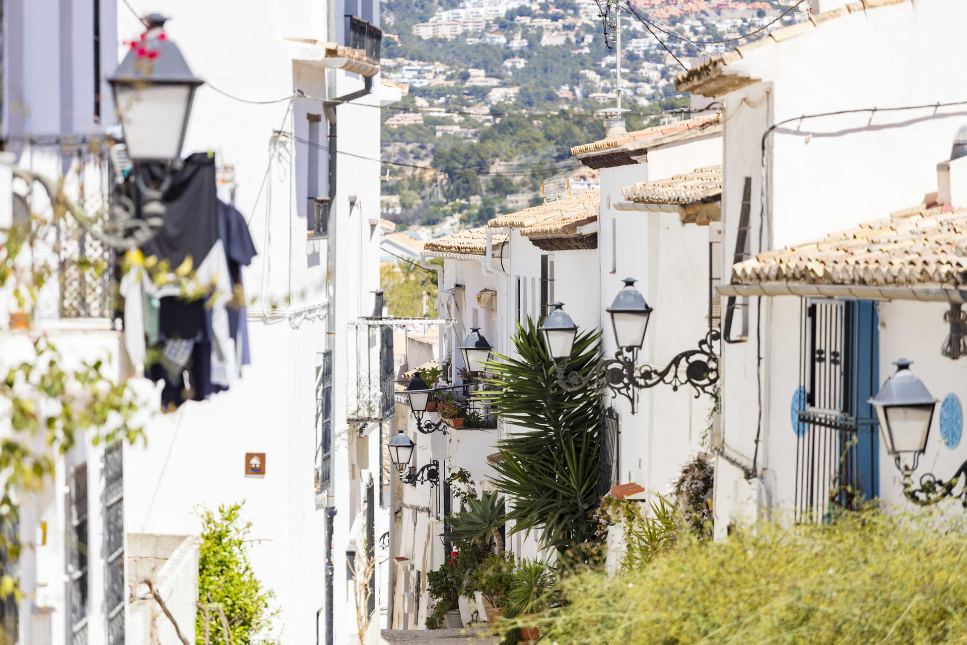 View of a traditional narrow street in Altea featuring white-washed facades, wrought iron street lamps, and terracotta tiled roofs.