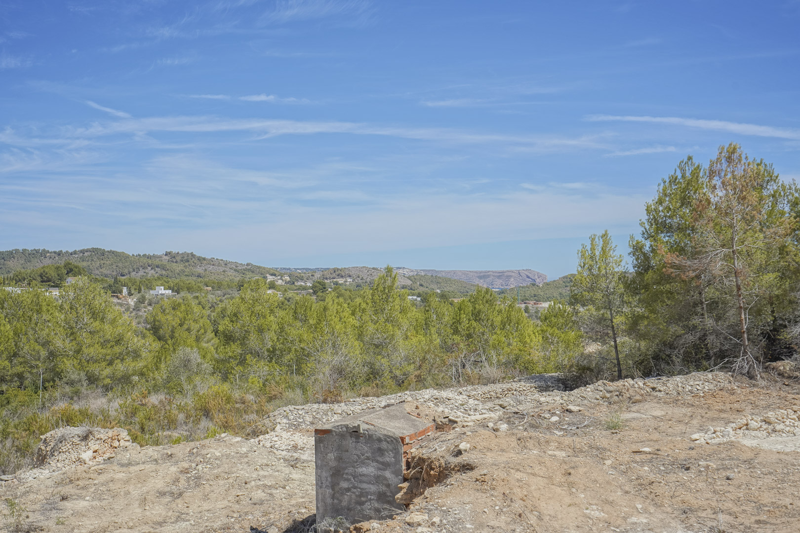 Elevated plot view showcasing the natural Mediterranean landscape with pine trees and distant mountain ranges under a clear blue sky.