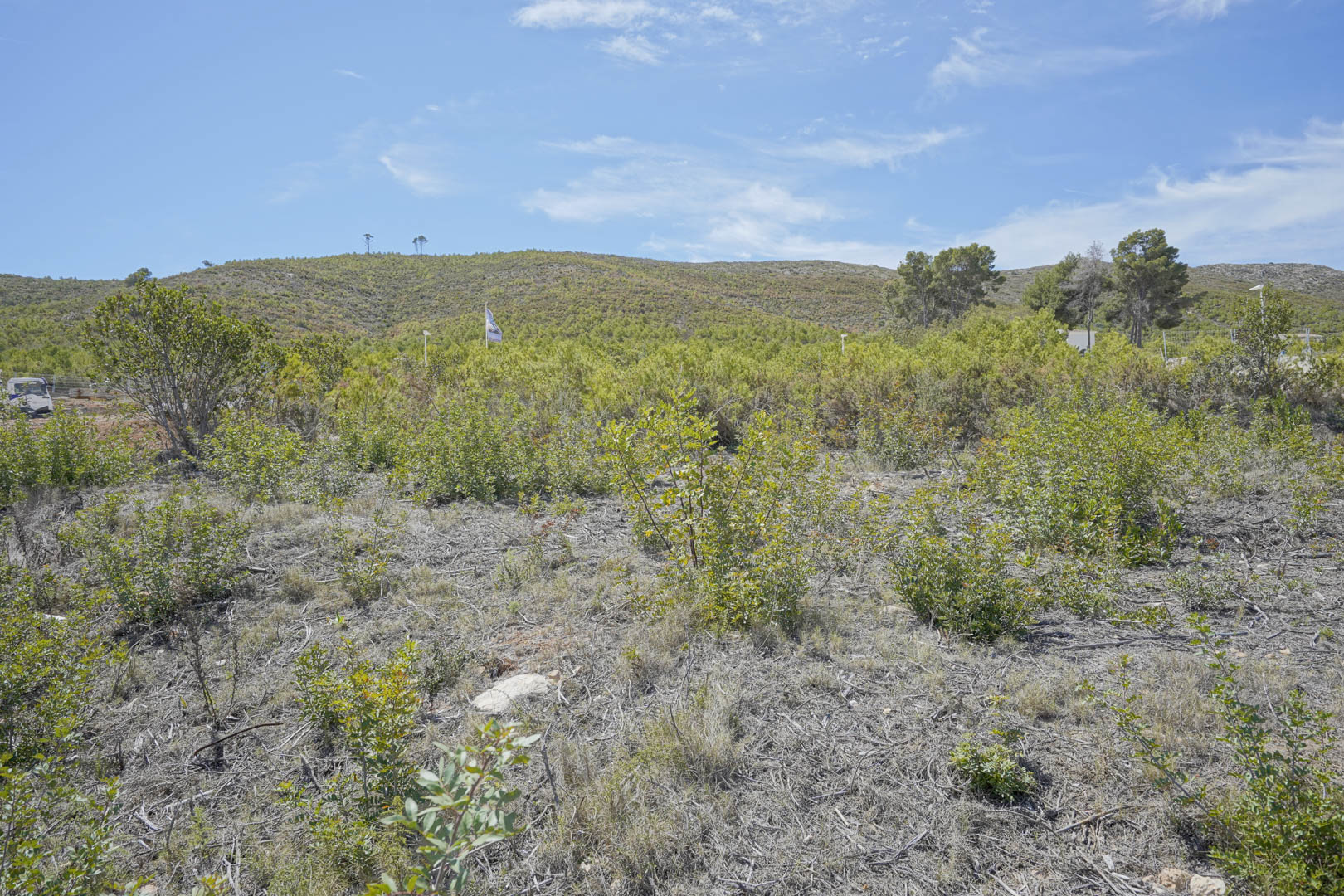 A 1514 m2 building plot featuring natural Mediterranean shrubland and panoramic views of the surrounding hills and clear blue sky.