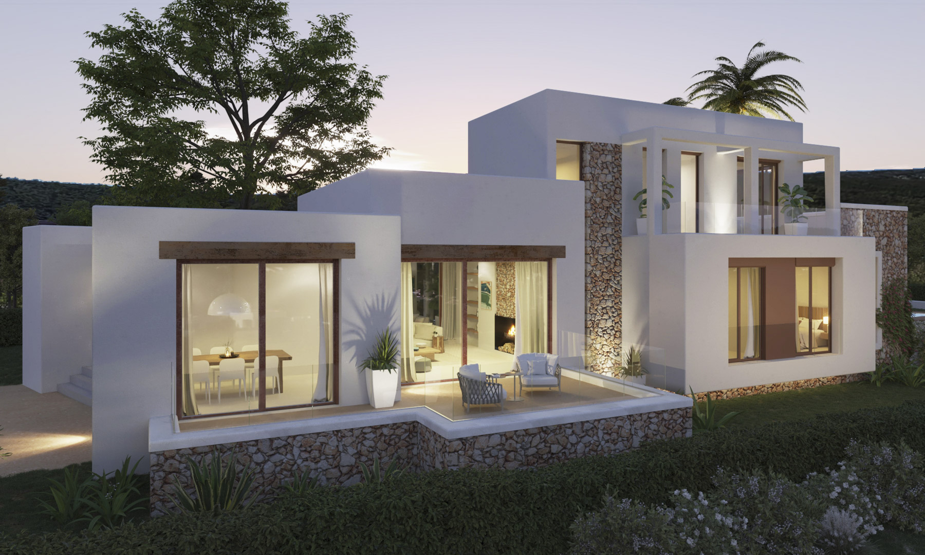 Ibizan-style facade featuring natural stone accents and white walls. The elevated terrace with glass railings connects the illuminated living areas to the Mediterranean garden.