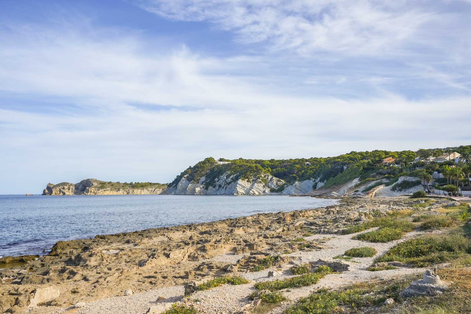 Panoramic view of the rocky Jávea coastline, featuring limestone cliffs and the Mediterranean shore under a clear sky.