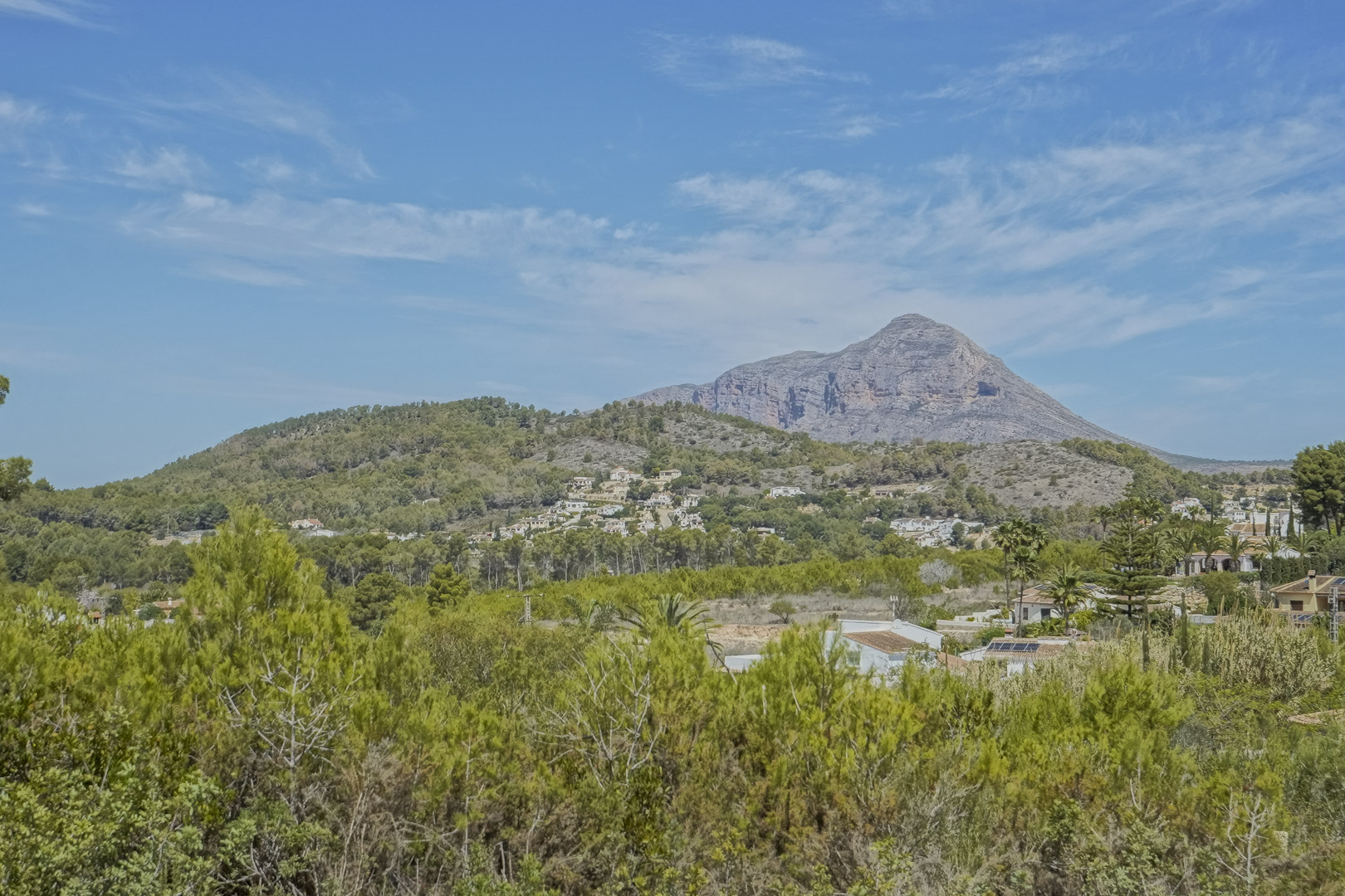 Panoramic views of the Montgó mountain and the surrounding Mediterranean landscape, featuring lush pine forests and scattered villas under a clear blue sky.