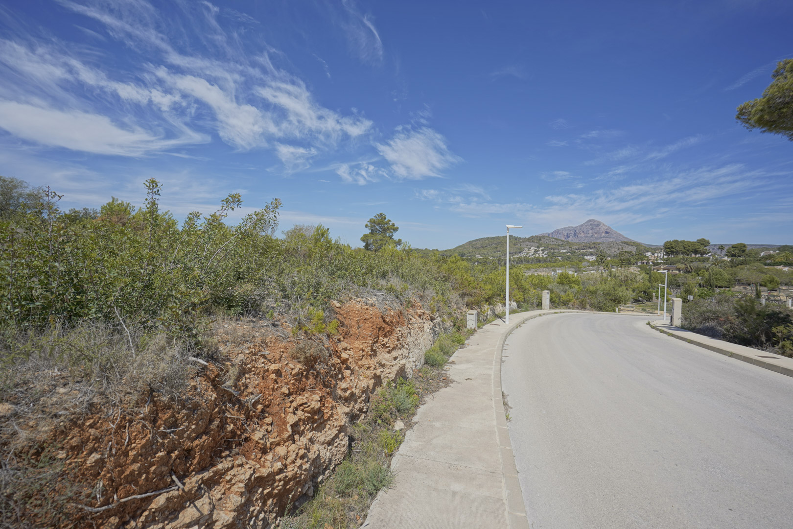 View of the access road in the Valsol residential area of Jávea, featuring the Montgó mountain in the distance and native Mediterranean greenery.
