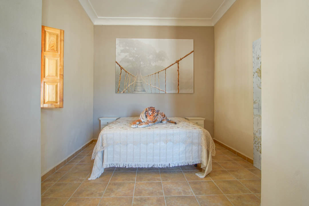 Bedroom featuring ceramic tile flooring, a double bed with white nightstands, and a window with traditional wooden shutters.