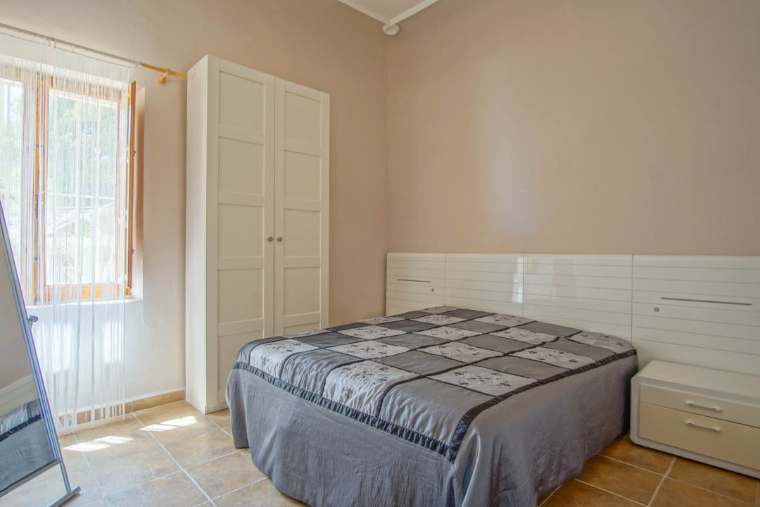 Bedroom featuring ceramic tile flooring, a freestanding white wardrobe, and a modern headboard with integrated storage and natural light.