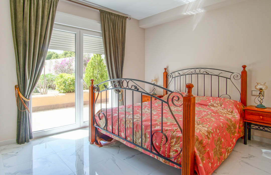 Bedroom featuring polished marble-effect flooring, a wrought-iron bed frame, and direct access to a garden terrace through large glass doors.