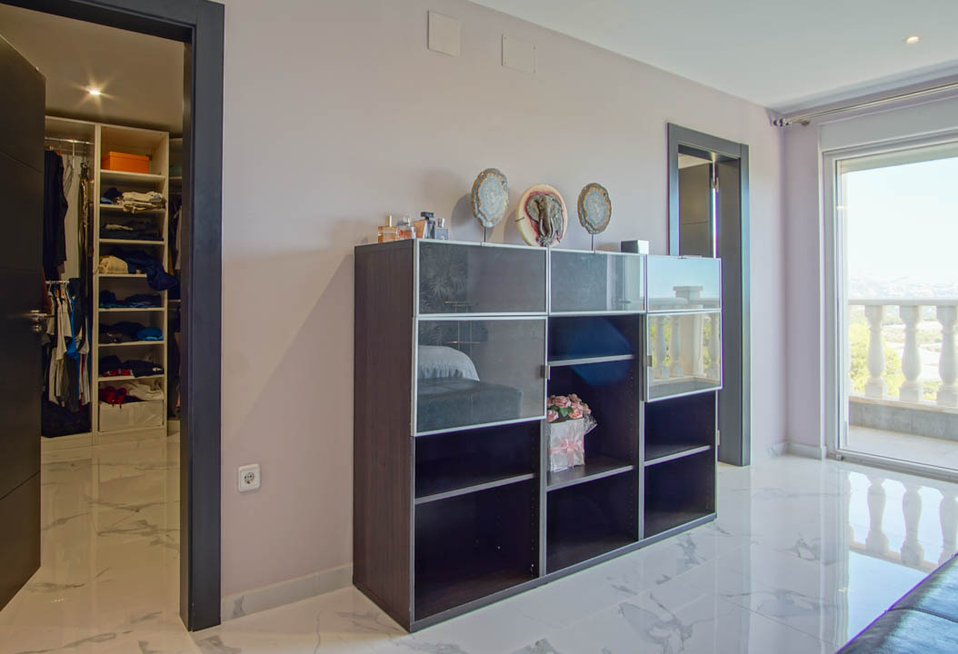 Bedroom featuring white marble floors, a walk-in closet with integrated shelving, and access to a balcony with stone balustrades.