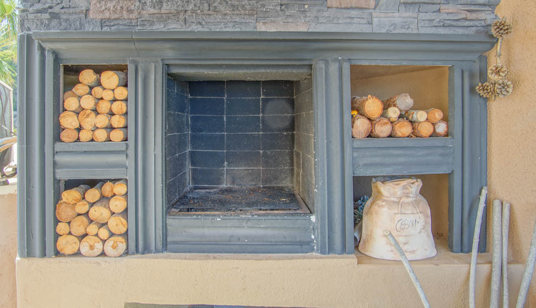 Built-in outdoor fireplace featuring a central grill, stone cladding, and dedicated side compartments for firewood storage.