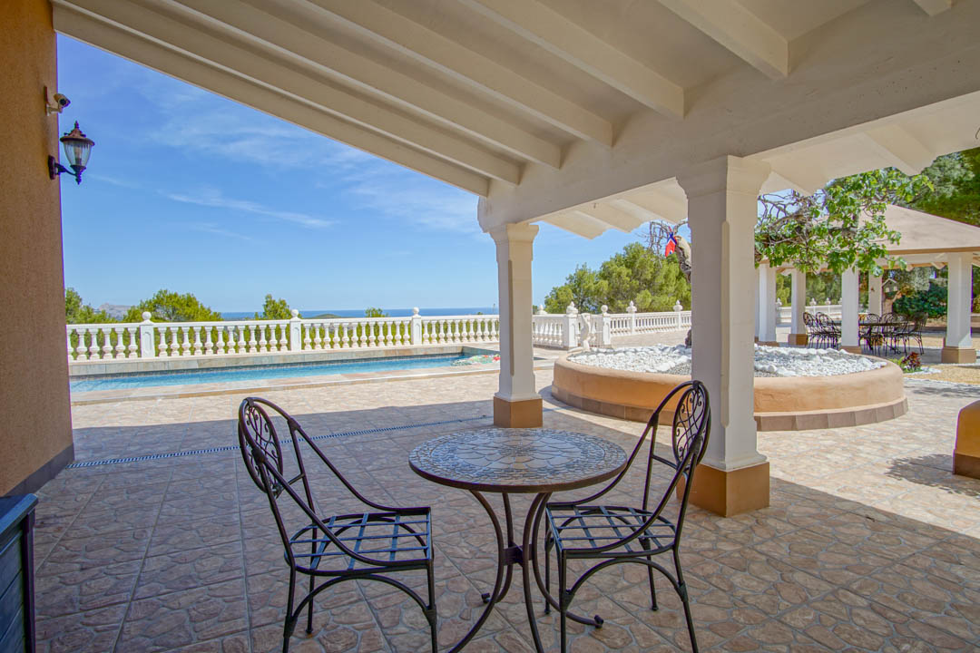 Covered terrace featuring a white beamed ceiling, wrought iron furniture, and panoramic views of the pool and sea.