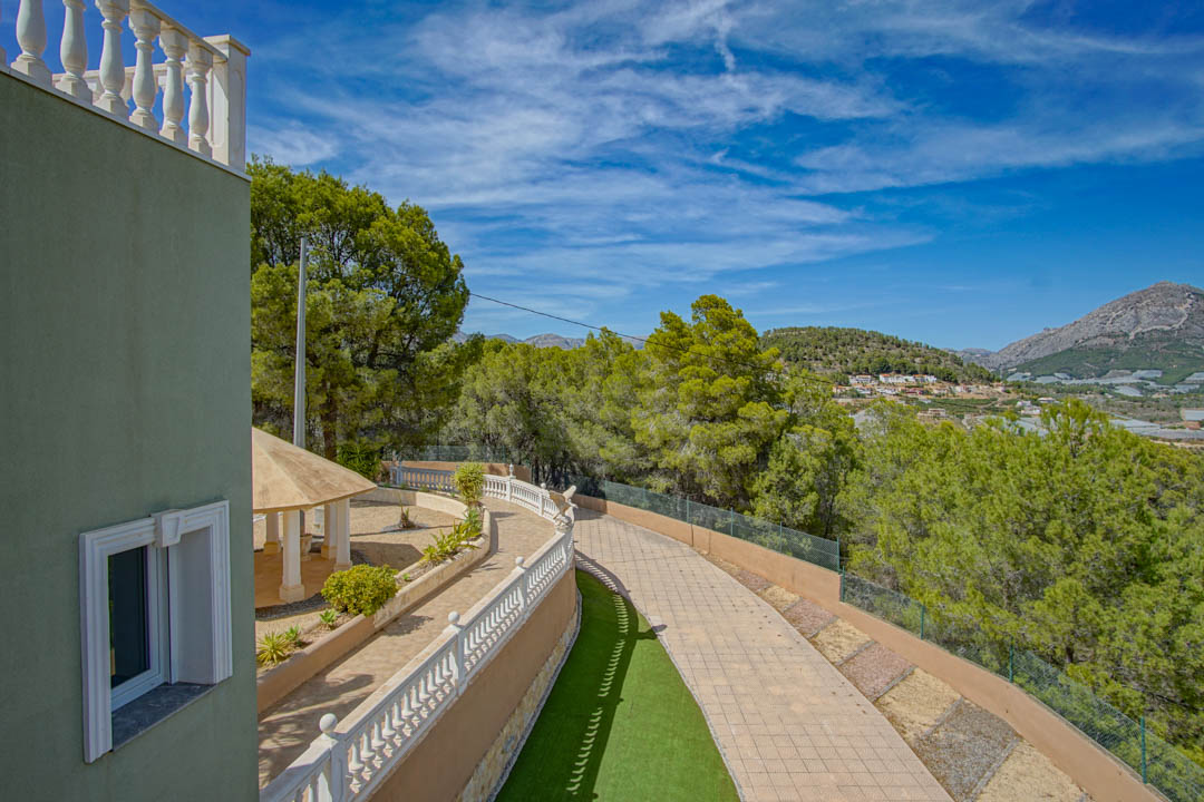 Elevated view of the paved driveway and classic white balustrades. A shaded pavilion sits within landscaped grounds, surrounded by pine trees and mountain vistas.