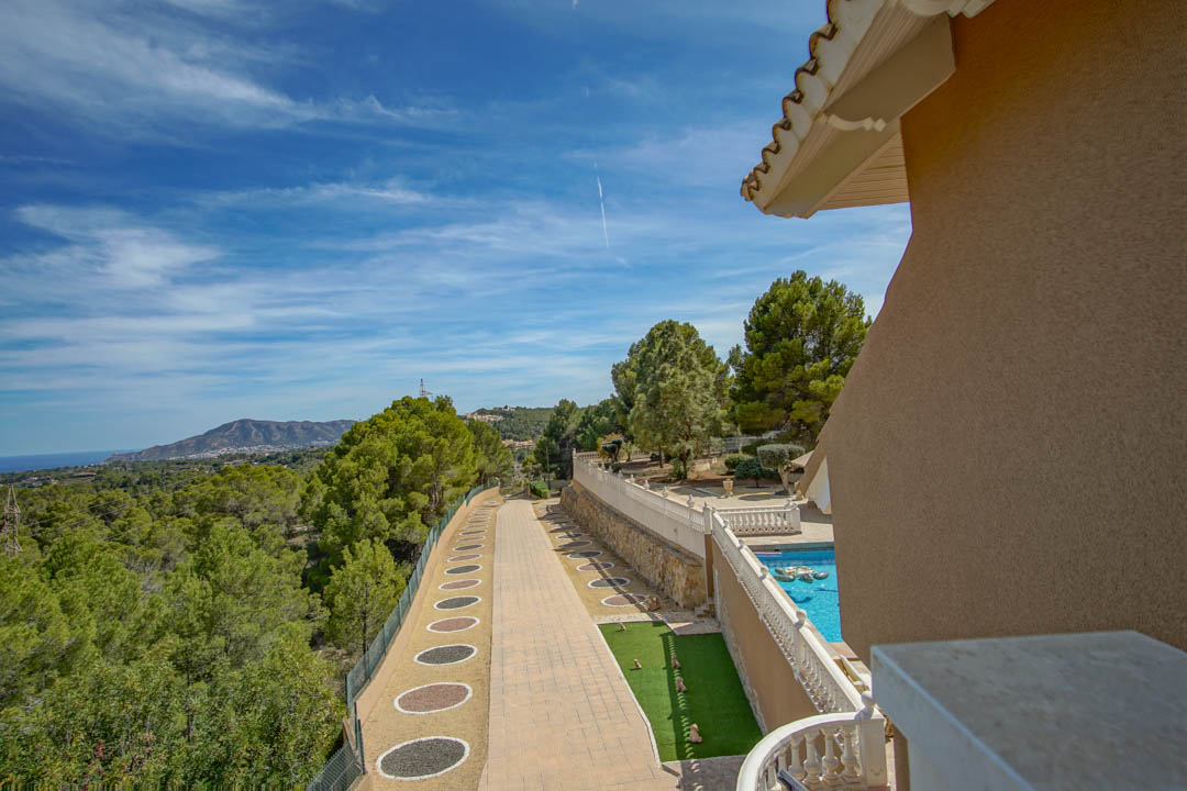 Elevated view showing the paved driveway with decorative gravel, the pool area with white balustrades, and panoramic vistas of the Mediterranean Sea and mountains.