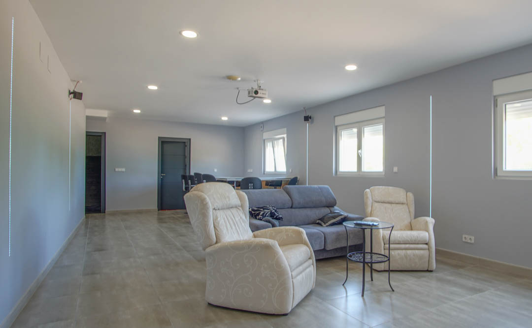 Entertainment and cinema room featuring a ceiling projector, lounge seating, and a background bar area with recessed lighting and tiled flooring.