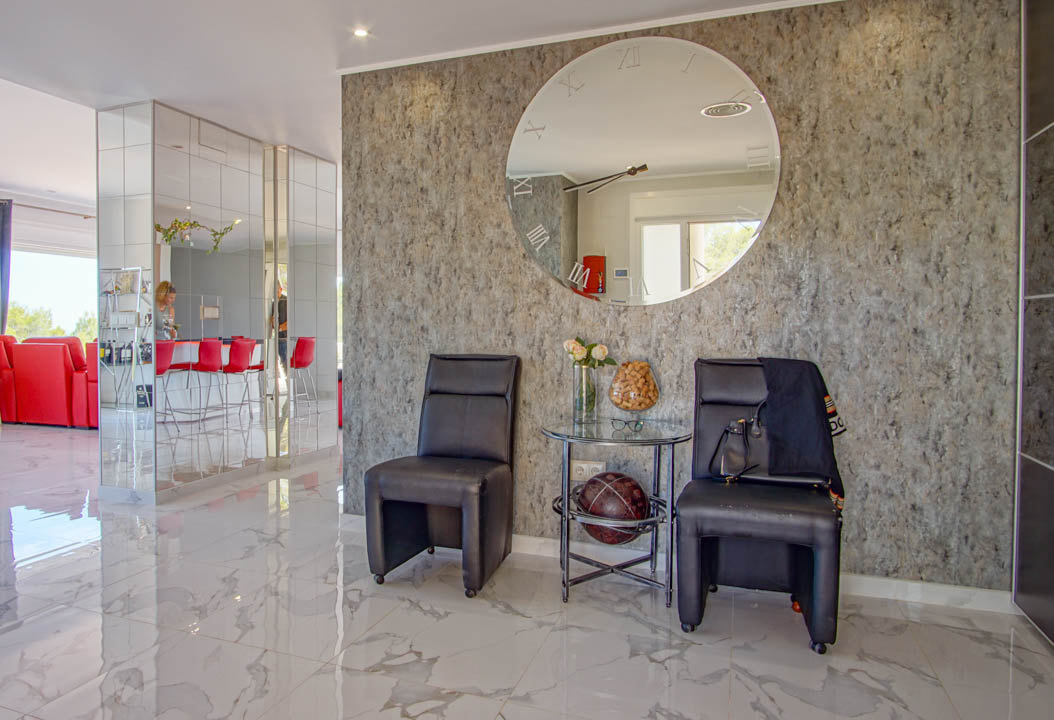 Entrance area featuring polished marble floors, a textured grey accent wall with a large circular mirror, and mirrored columns reflecting the open-plan layout.