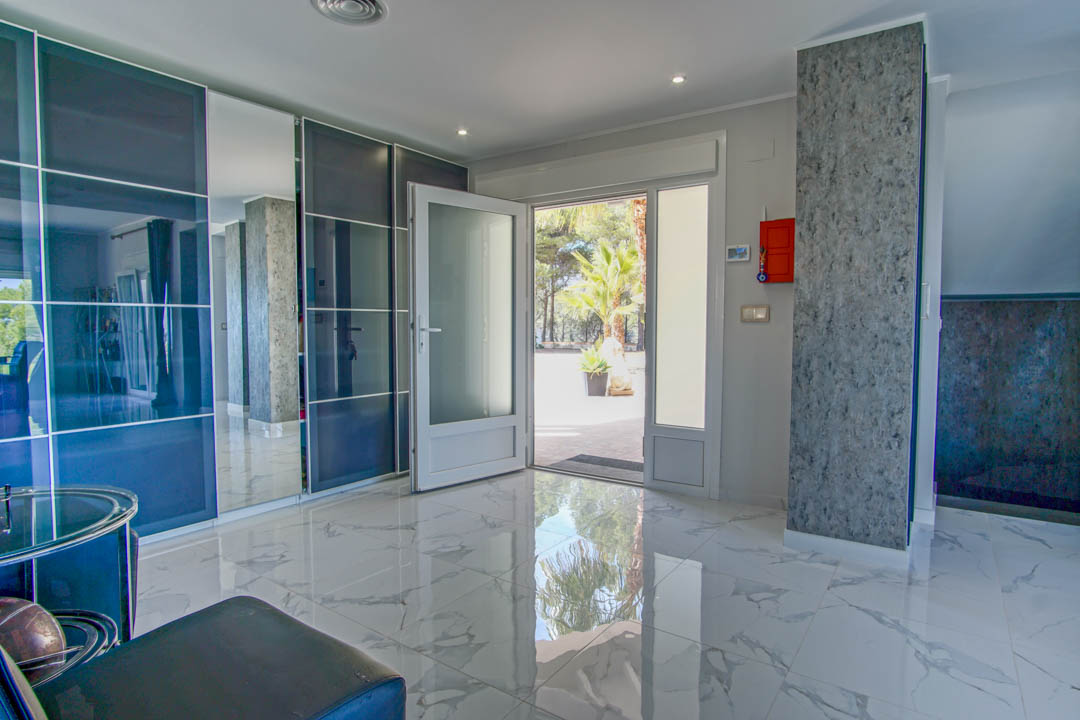 Entrance foyer featuring polished marble-effect flooring, integrated smoked glass wardrobes, and a glass door opening to the sunlit exterior.