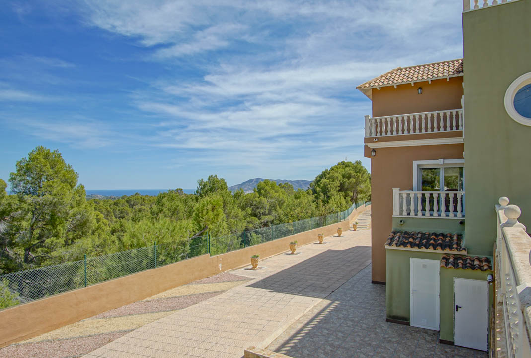 Exterior view featuring the multi-level facade with balustrade balconies, a paved pathway, and expansive views over the pine forest toward the Mediterranean Sea.