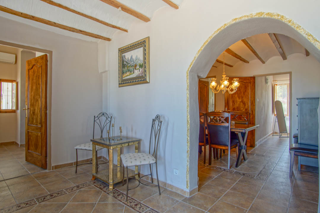 Hallway featuring exposed wooden ceiling beams and tiled floors with decorative borders, leading to the dining area through a textured arch.