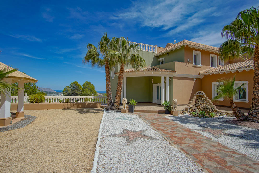 Main entrance featuring star-patterned pebble mosaics, palm trees, and sea views. The facade blends earthy tones with white columns and stone decor.