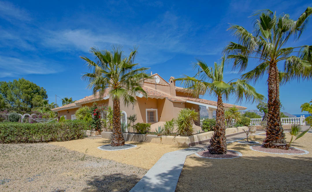 Mediterranean exterior featuring earth-toned walls and tiled roofing, set within gravel gardens with mature palm trees and paved walkways.