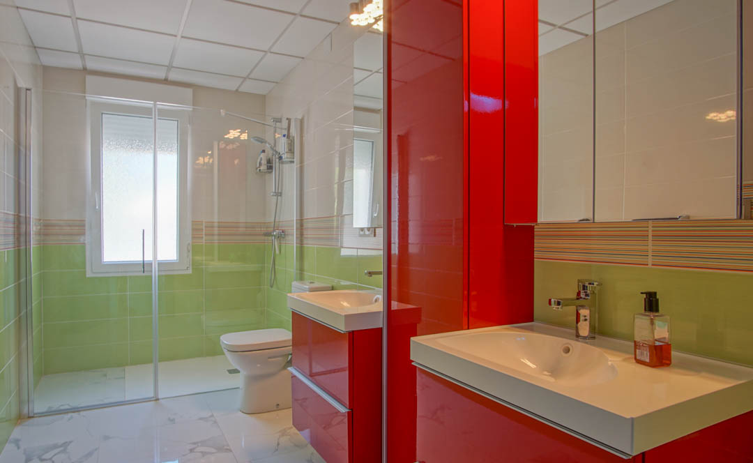 Modern bathroom featuring a vibrant red high-gloss vanity, walk-in glass shower, and lime green wall tiling with marble-effect floor tiles.