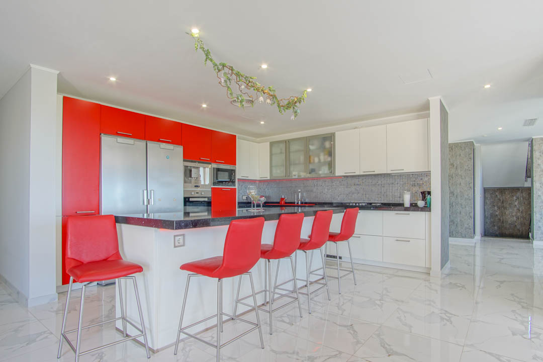 Modern kitchen featuring a black granite island with red bar stools and high-gloss cabinetry. Large white marble floor tiles and integrated stainless steel appliances.