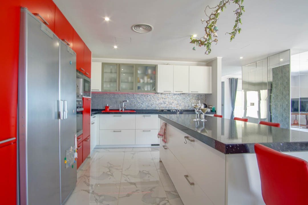 Modern kitchen featuring high-gloss red and white cabinetry, a spacious island with a dark countertop, and polished marble-effect flooring.