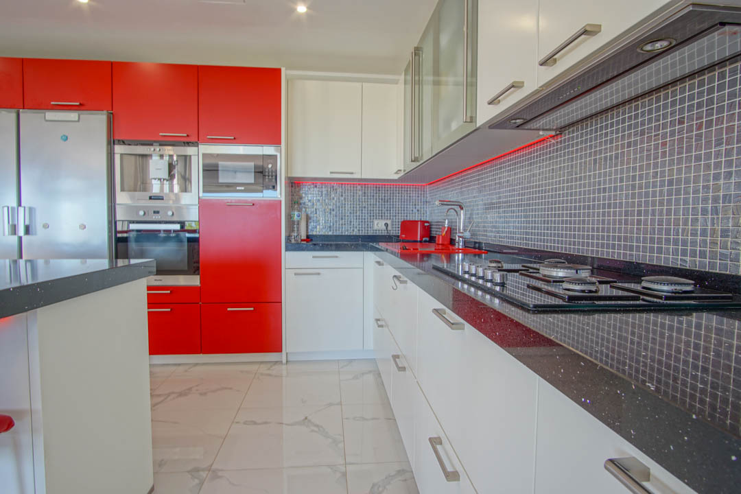 Modern kitchen featuring high-gloss red and white cabinetry, black granite countertops, and a grey mosaic backsplash with integrated LED lighting.